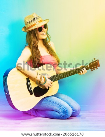 Teenager girl guitar play sitting on a floor. Blue wall  background. Country style.