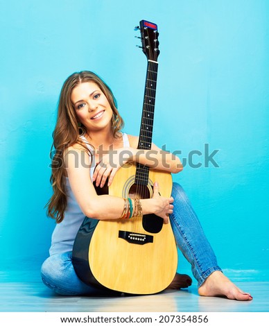 Young woman musician with guitar sitting on a floor. Blue background.
