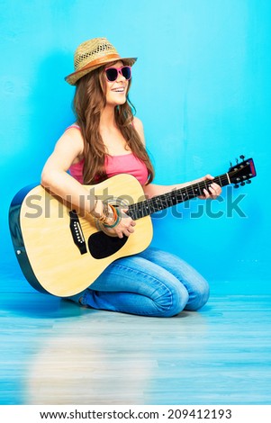 Teenager girl guitar play sitting on a floor. Blue wall  background. Country style.