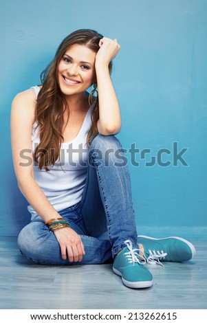 young smiling woman sitting on floor against blue wall . hipster style .