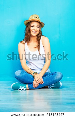 young woman with long curly hair sitting on floor against blue wall . female portrait .  crossed leg
