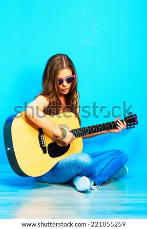 young woman sings and playing guitar . sitting against blue