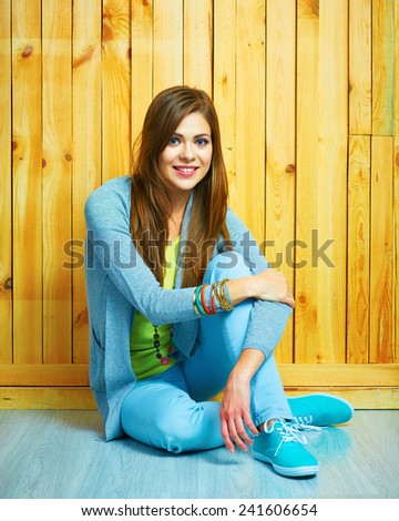 Smiling teenager style dressed girl sitting on a floor with crossed legs. Young woman portrait.