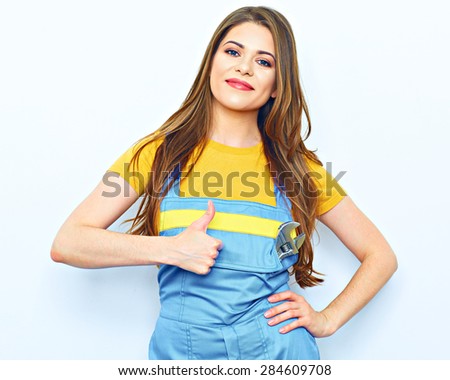 Young woman worker in coveralls show thumb up. Female smiling model with long hair.
