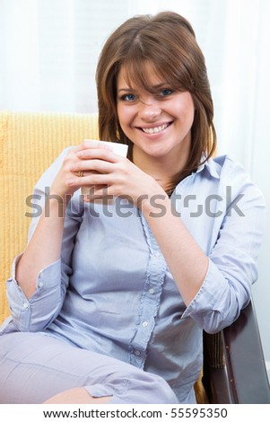Portrait of happy young woman  while sitting on chair at home with coffee cup