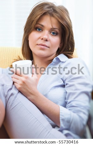 Portrait of happy young woman  while sitting on chair at home with coffee cup