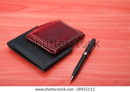 Two leather purse lies on a wooden table. Near to purse  pen  lies.