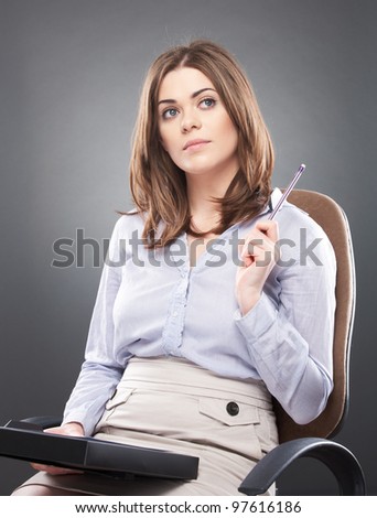 Young business woman [ student ] sits in office chair with pen, isolated on gray