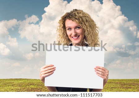 Attractive young business woman with curly hair holding a blank poster against rural background.