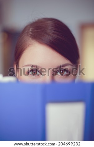 Portrait of young caucasian business woman peeping out from blue ring binder