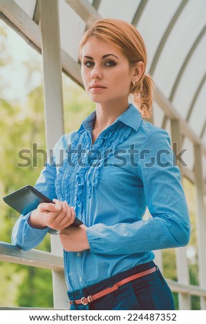 Business woman in a blue striped shirt with tablet pc leaning against the frame of the balcony