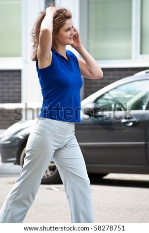 Young woman speaks by phone, walking on a parking outside of office building