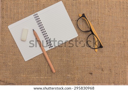 note book ,pencils,eraser,glasses on sack background