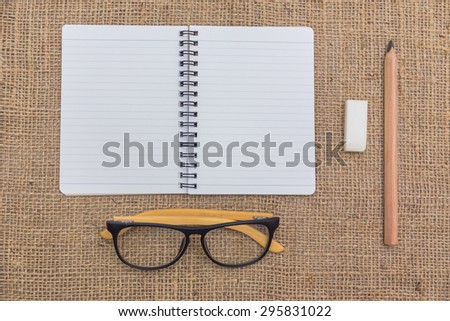 note book ,pencils , glasses and rubber on sack background