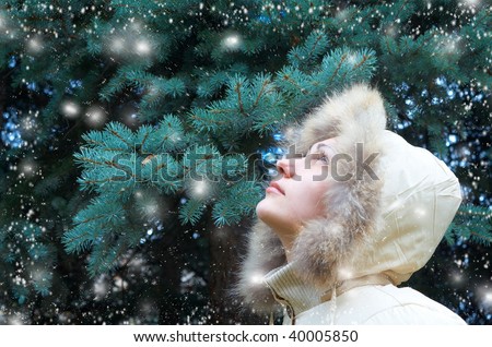Beautiful girl in a winter jacket, looks up at the tree and coming snow. Insert text or item in the place where the girl looks