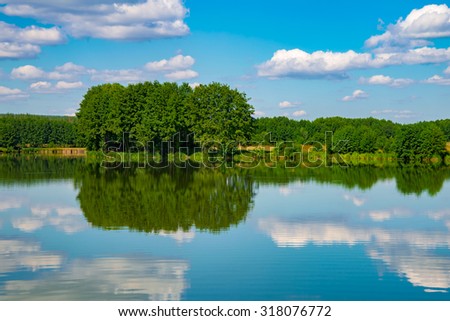 Green trees on the banks of the river. Reflection of clouds in water.