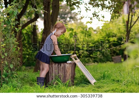 little helper girl washes dress in a basin outside, the girl in a striped dress