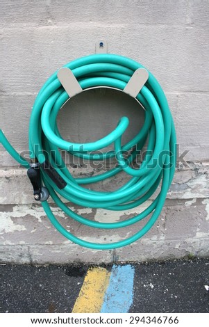 Green Garden Water Hose Coil Wrapped and Hung on Cement Wall