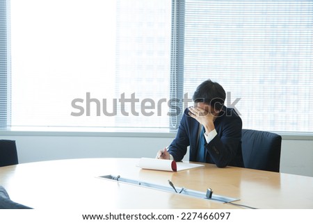 A business man covering his face in a office room (looking down)