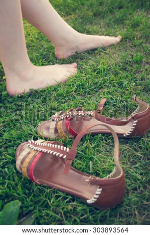 Bare female legs on grass near stand sandals. Selective focus, Image tinted