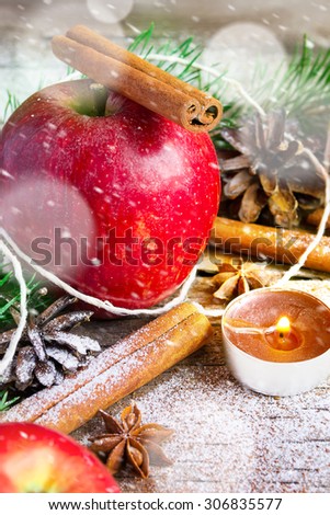 Christmas composition: Apple, candle and cinnamon sticks. Snowing.
