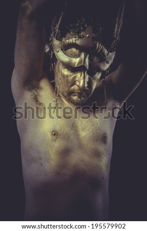 Man with body painted gold feather mask and steel sword