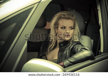 blonde in car driving at night, dressed in jeans and leather jacket