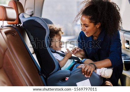 Happy mother looking at her son in a baby seat. Young female preparing kid for a trip. Stock foto © 