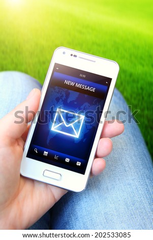 mobile phone with message holded by hand with green field as a background. focus on screen
