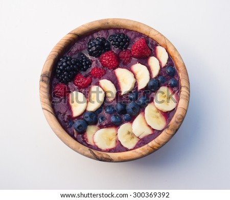 berry acai smoothie bowl in a wooden bowl topped with bananas, blueberries, blackberries and raspberries