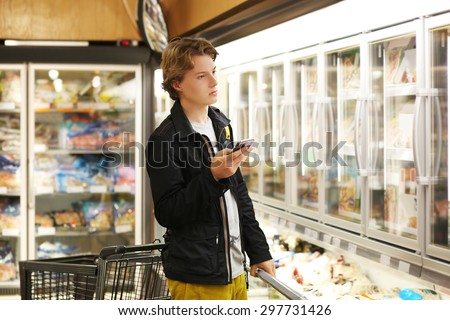 Young man choosing frozen food from a supermarket freezer. Checking list.