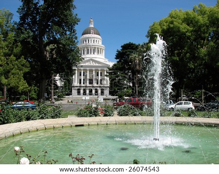 California State Capital in Sacramento on a perfect day with green trees and blue sky framing the white building through a fountain