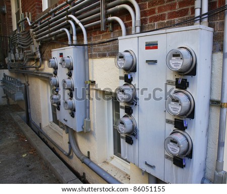 Several rows of electric and gas meters on the side of a brick apartment