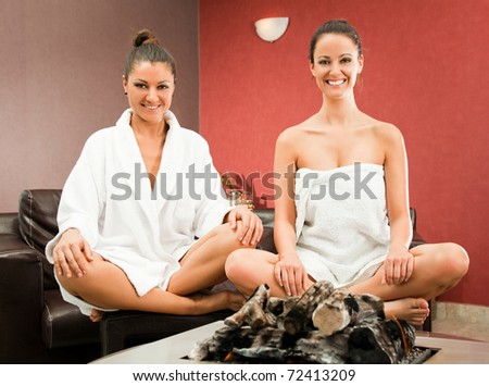 Two happy women sitting in lotus position behind modern fireplace