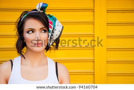 Beautiful female with colourful make-up on yellow background, looking left