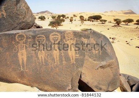 Ancient rock art in Niger depicting four round headed figures and animals in the Sahara desert