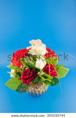 White and red Artificial flowers are carnation and rose in a vase on blue plate