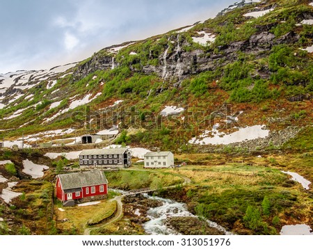 ?utumn landscape with traditional Norwegian mountain village with snow caps on the meadow with river, Sognefjord, Norway