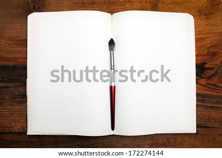 Open book on wooden table with paint brush.
