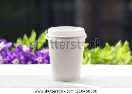 Disposable coffee cup on windowsill with a city in background.