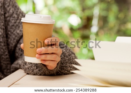 Morning coffee and a book. Woman holds a disposable coffee cup while reading a book
