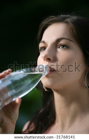 Beautiful young woman in the park. Drinks water.