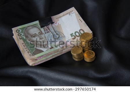 bundle of bank notes and stacks of coins on black leather