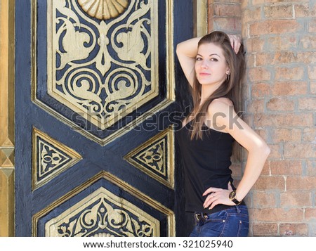 Portrait of a young girl, the girl on a walk around town, everyday makeup, wooden door with gold decoration, long hair, brick wall, jewelry made of gold.
