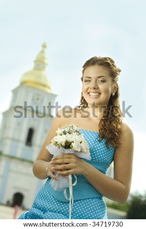 Laughing bride holding flovers, church behind her back.