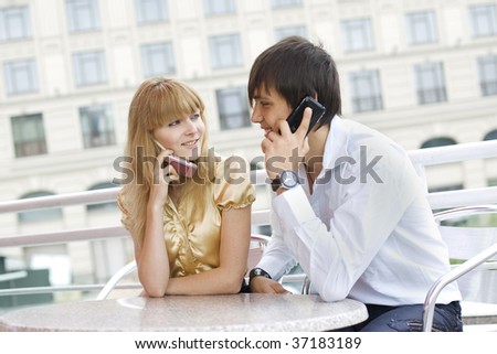 Young couple sitting in the cafe, both talking on their cell phones