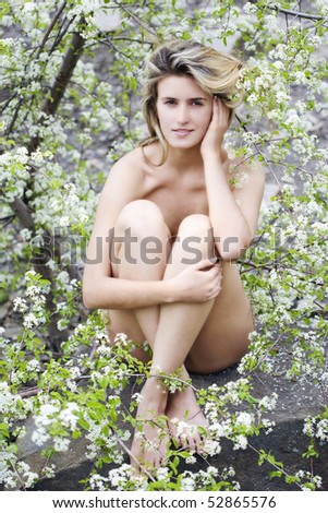 Young naked woman on the stone in the bloom of fruit tree.