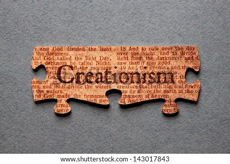 The word Creationism against background of Genesis text printed on matched jigsaw pieces.