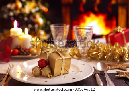 A romantic Christmas dinner table setting with candles and Christmas decorations. A fire is burning in the fireplace and Christmas stockings are hanging on the mantelpiece.