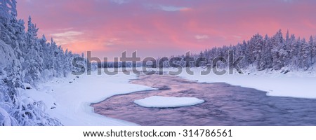 A rapid in a river in a wintry landscape. Photographed at the Äijäkoski rapids in the Muonionjoki river in Finnish Lapland at sunrise.